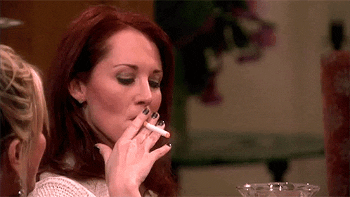 a woman is smoking a cigarette while sitting at a table