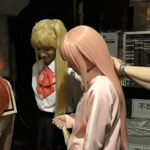 a woman in a pink jacket is standing next to a woman in a blonde wig