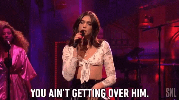 a woman in a crop top is singing into a microphone on stage .