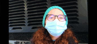 a woman wearing a face mask and glasses is standing in front of a fan