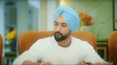 a man wearing a blue turban and a white shirt is sitting at a table .