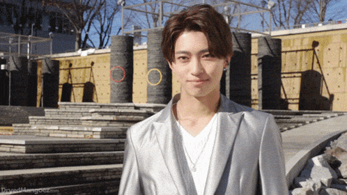 a young man wearing a silver jacket and a white shirt is standing in front of a wall with circles on it