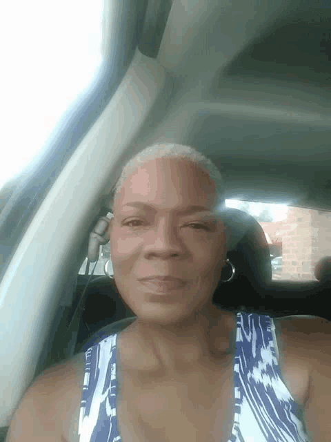a woman in a blue and white tank top smiles in a car