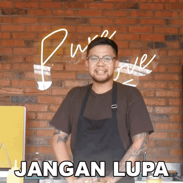 a man in an apron is standing in front of a brick wall with the words jangan lupa written on it