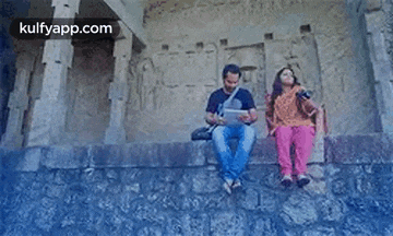 a man and a woman are sitting on a stone wall . the woman is holding a camera .