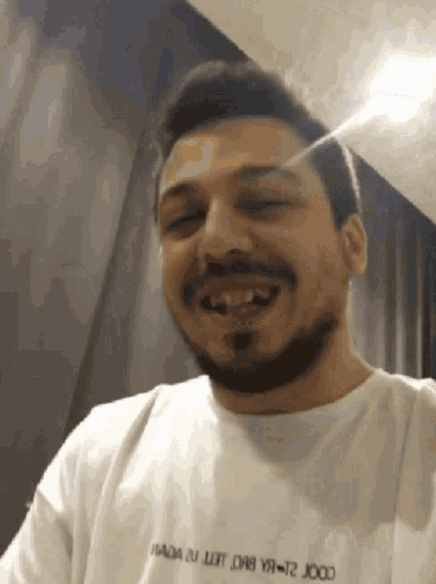 a man with a beard is smiling and wearing a white shirt with the word prada on it