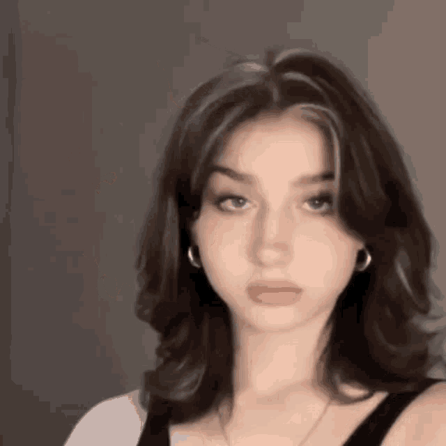 the girl is wearing a black tank top and earrings and has a very short haircut .