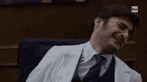 a man in a white coat and tie is sitting in a chair with his eyes closed .