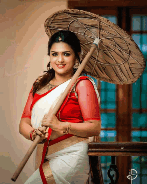 a woman in a red and white saree holds a large umbrella