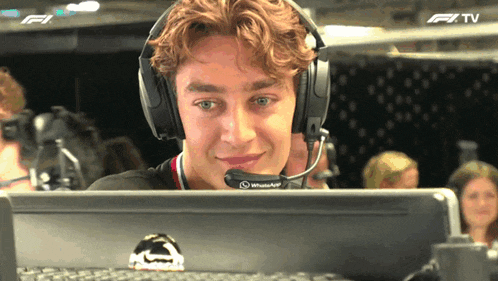 a man wearing headphones and a microphone is looking at a computer screen with a f1 tv logo in the background