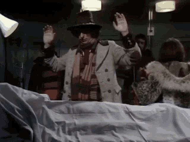 a man in a hat and coat is standing in front of a corpse .