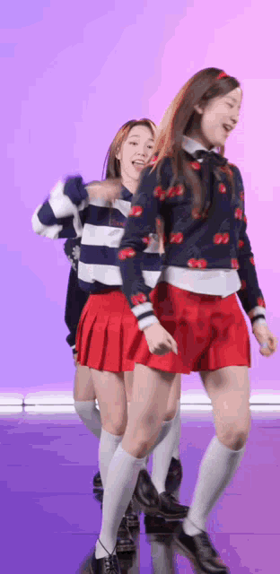 two girls in red skirts and white socks are dancing in front of a purple background