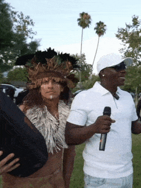a man in a white shirt is holding a microphone next to a man in a native american outfit