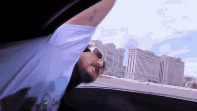 a man wearing sunglasses is sitting in a car with his arms out the window .