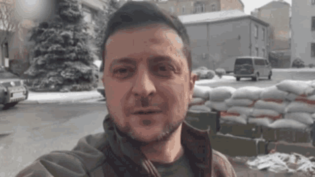 a man with a beard is standing in front of a pile of sandbags in the snow