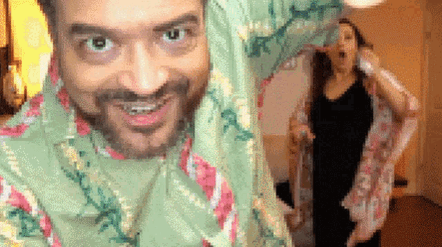 a man with a scarf around his head is smiling while a woman stands in the background