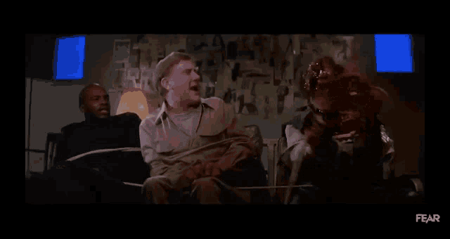 a group of men are tied up and sitting in chairs in a room in a movie .