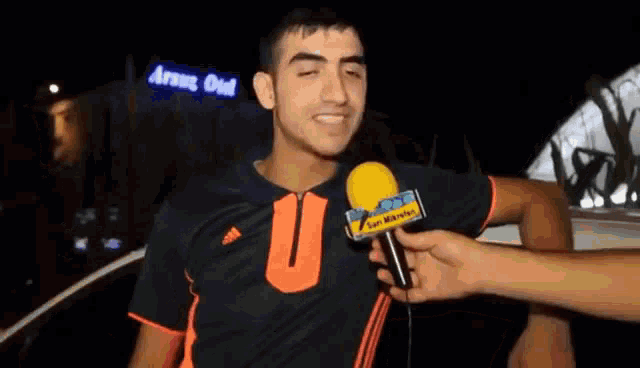 a man in an adidas shirt is being interviewed by someone with a yellow microphone