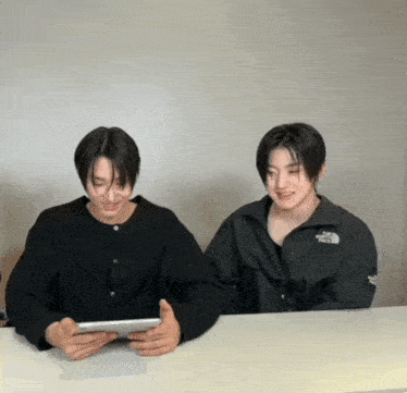 two young men wearing the north face jackets are sitting at a table