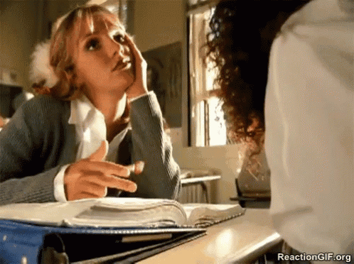 a woman is sitting at a desk with a book in front of her talking to another woman .