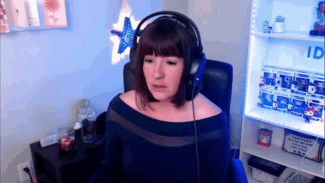 a woman wearing headphones is sitting in front of a shelf that says ' vid ' on it
