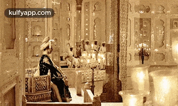 a man in a costume is sitting on a throne in a room filled with candles .