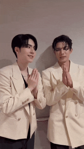 two men in white suits are standing next to each other with their hands folded .
