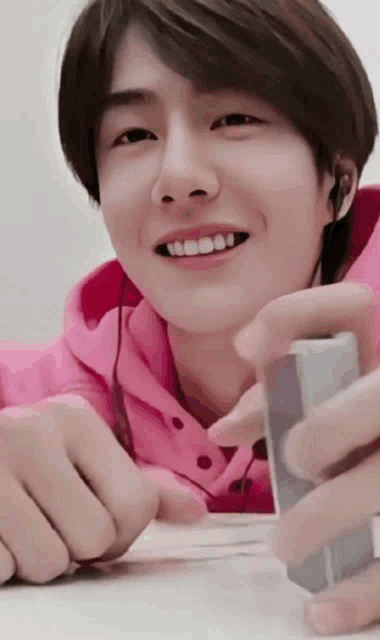a young man wearing a pink hoodie is smiling and holding a lighter