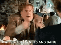 a man is sitting at a table talking to another man while eating donuts .