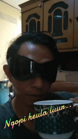 a man wearing blindfolds is holding a cup of coffee with the words ngopi heula tuun written on it