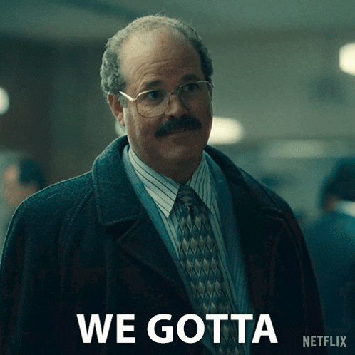 a man with glasses and a mustache is standing in front of a sign that says we gotta