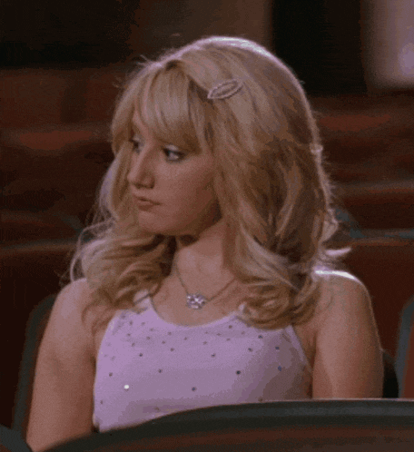 a blonde woman wearing a pink top and a necklace