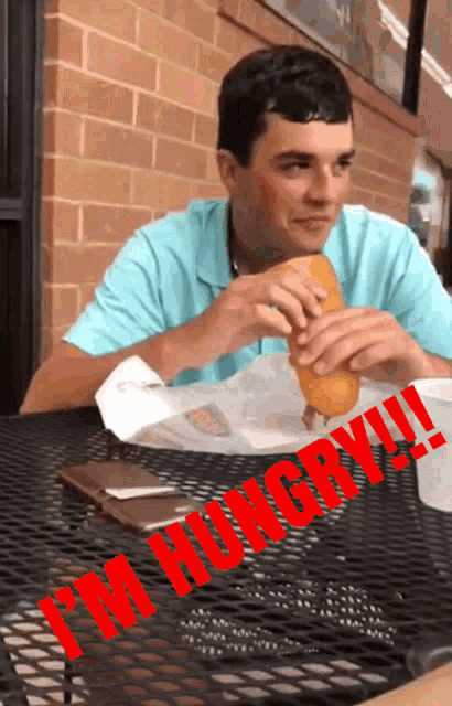 a man is sitting at a table eating a sandwich with the words " i 'm hungry " written on it
