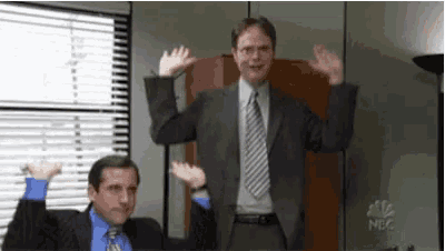 a man in a suit and tie is standing in front of a window with his hands in the air .