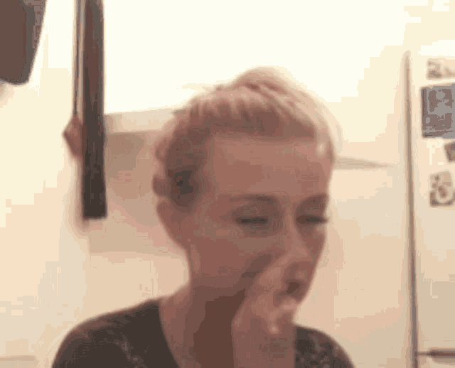 a woman is covering her nose with her hand while sitting in front of a refrigerator .