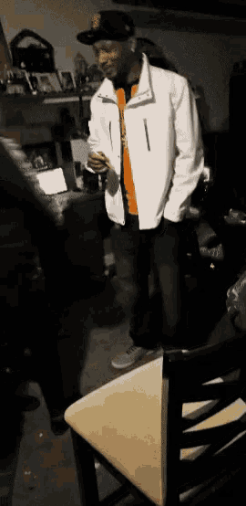 a man wearing a white jacket and a san francisco giants hat stands in a dark room