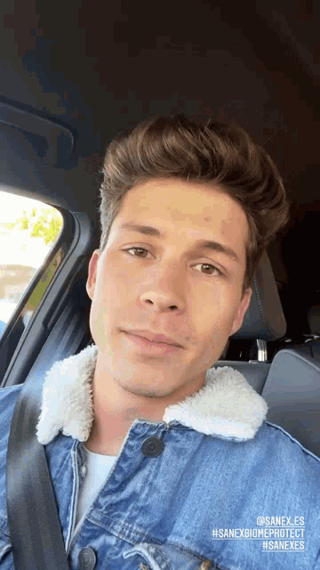 a young man wearing a denim jacket is sitting in a car
