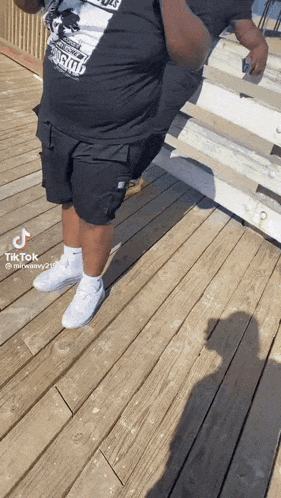 a man is standing on a wooden deck wearing a black shirt and white shoes .