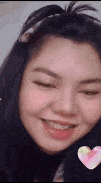 a woman with braces on her teeth is smiling with a heart in the background .