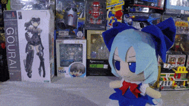 a doll with blue hair is sitting in front of a display of toys including a gourai figure