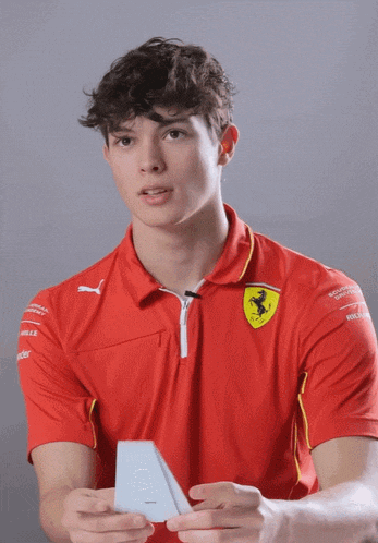 a young man wearing a red ferrari shirt holds something in his hand