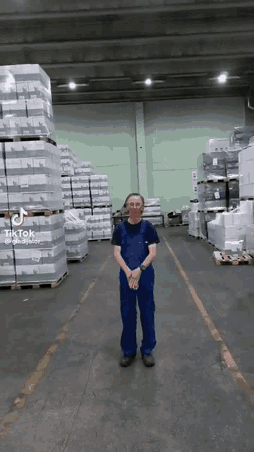 a man in blue overalls is standing in a warehouse with lots of boxes on pallets