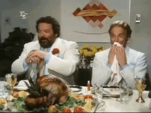 two men in suits are sitting at a table with a turkey on it .
