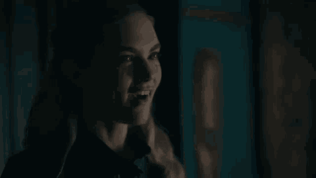 a woman is smiling in a dark room while looking at the camera .