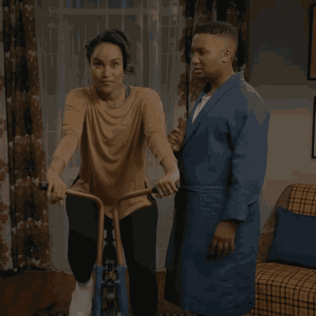 a woman is riding an exercise bike next to a man in a robe