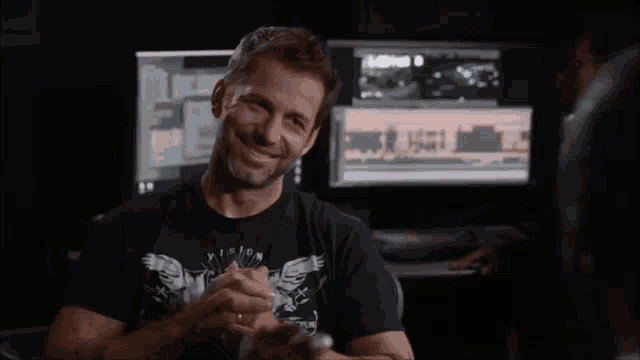 a man in a mission t-shirt is smiling in front of a computer monitor