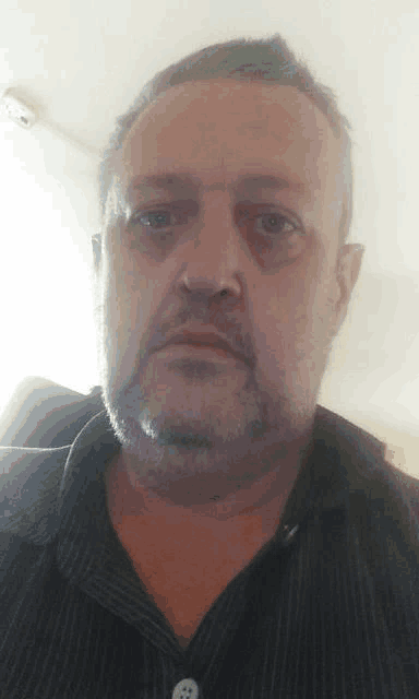 a man with a beard is wearing a striped shirt and looking at the camera