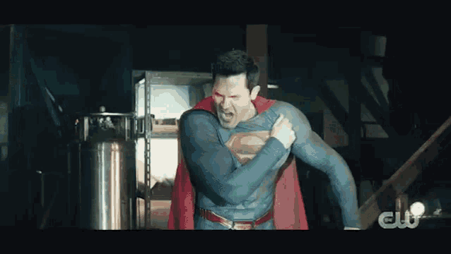 a man in a superman costume is standing in a dark room and holding his chest .