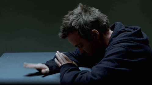 a man in a black hoodie sits on a table