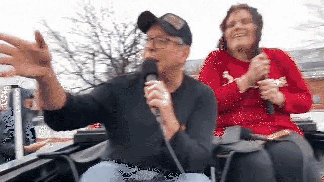 a man is singing into a microphone while a woman sits behind him .